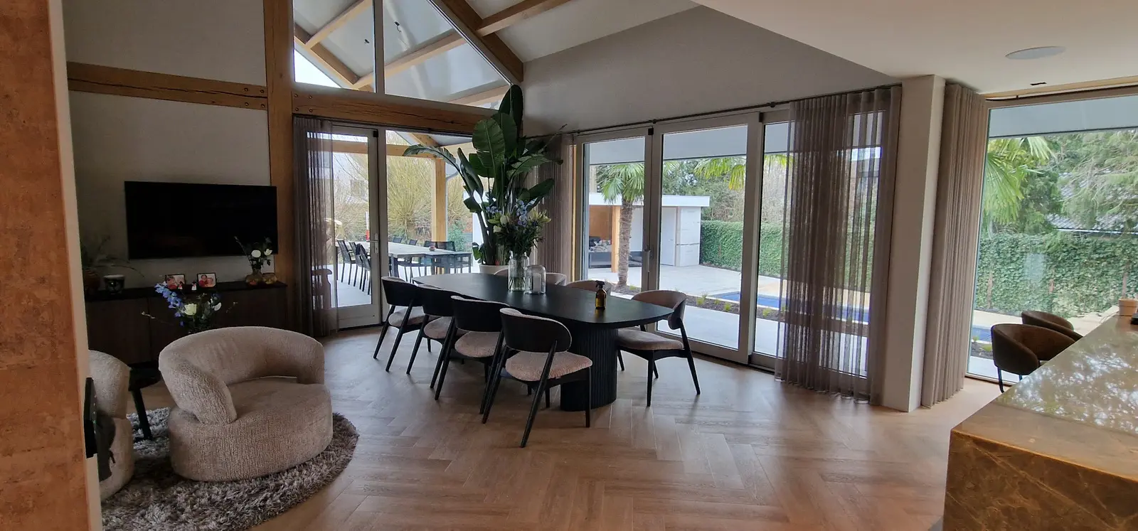 Eetzone onder de hoge kap met eikenhouten spanten en zicht op de tuinzijde