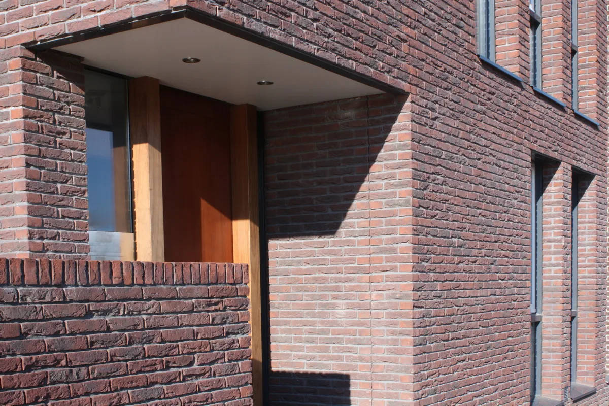 Geveldetail van torenwoning met ruwe baksteen en natuurlei met wisselende tinten in zonlicht