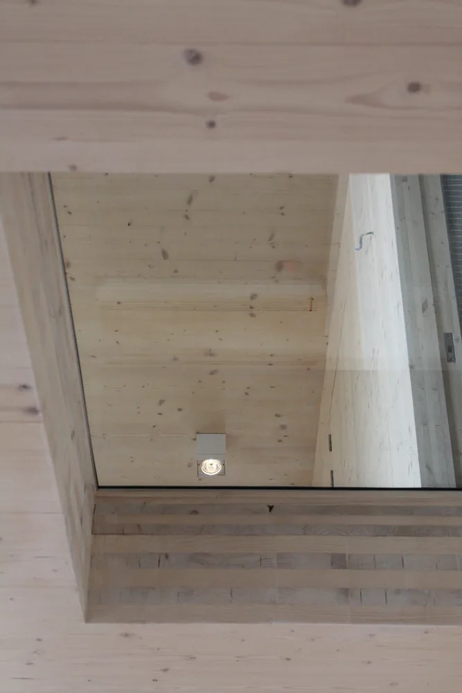 Woonkamer met zichtbare CLT-wanden, hoog daglicht en doorzicht naar de patio